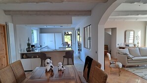 A spacious living area with a wooden dining table, wicker chairs, a sofa, and a kitchen in the background.