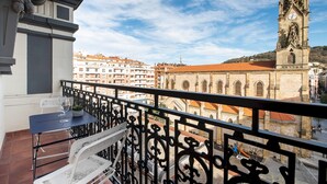 A balcony with a table, two chairs, and a potted plant. A clock tower is visible in the background. - Allegra by FeelFree Rentals (Donostia)
