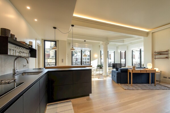 A modern kitchen with a central island, built-in appliances, and a large window offering a city view.
