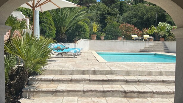 Ein Schwimmbecken mit Liegestühlen und einer Pergola mit Sonnenschirm.