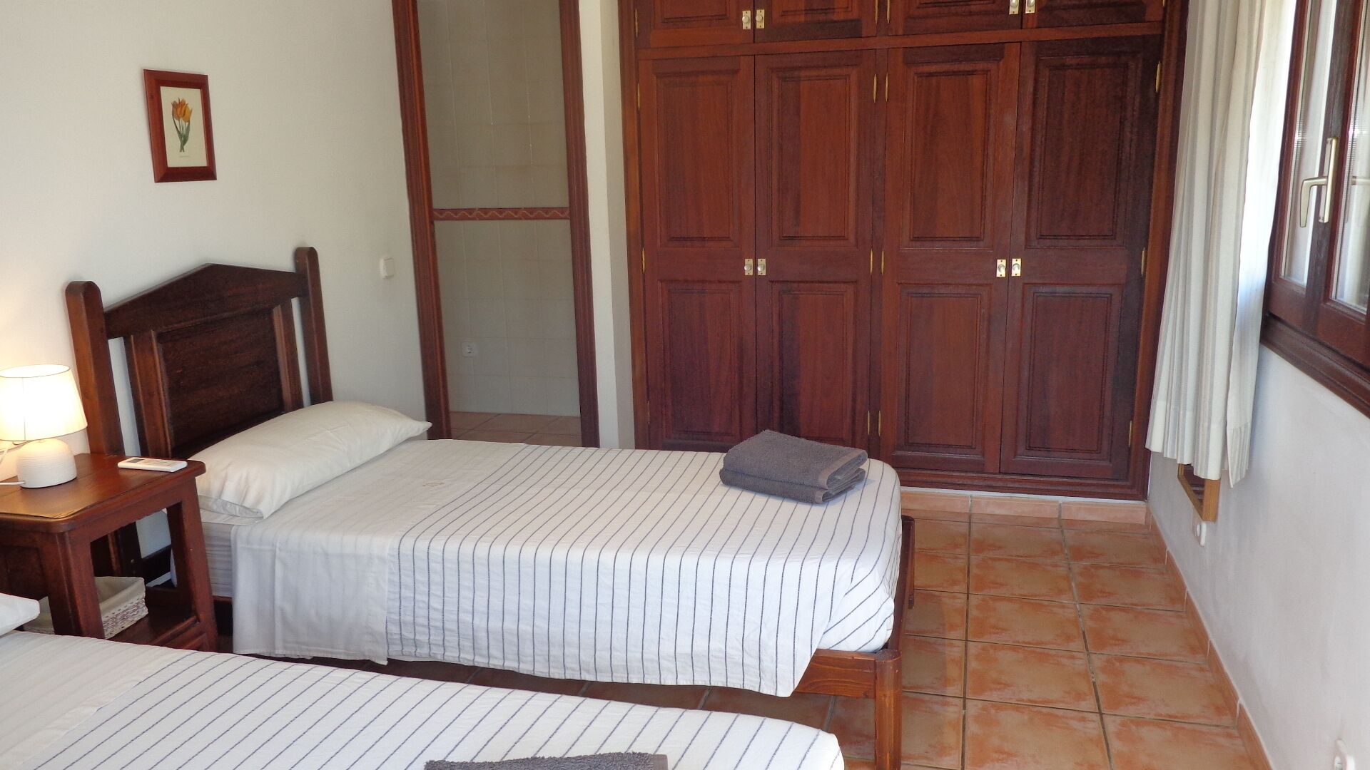 A bedroom with two beds, wooden wardrobe, and a nightstand with a lamp.