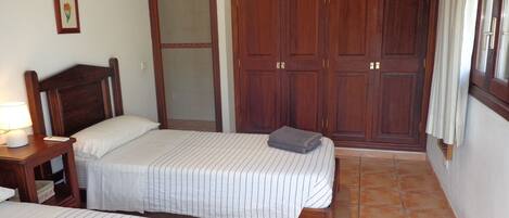 A bedroom with two beds, wooden wardrobe, and a nightstand with a lamp.