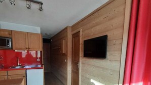 Kompakti keittiö, jonka seinät ovat puuta, seinälle asennettu taulutelevisio ja oikealla puolella punainen verho.