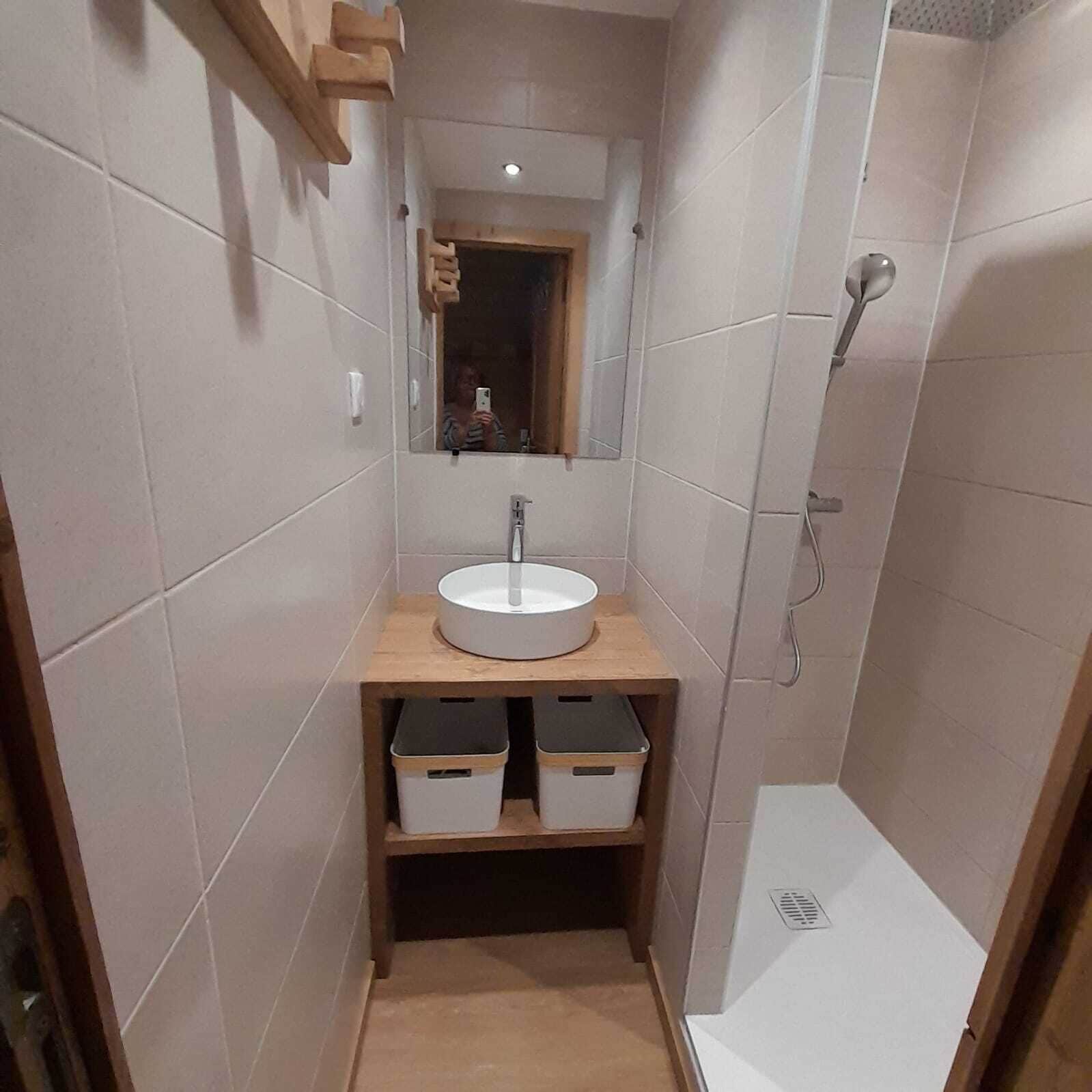 A small bathroom with a sink, mirror, and shower. There are storage boxes under the sink.