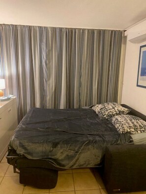 A bedroom with a bed, a nightstand, a lamp, and a curtain.
