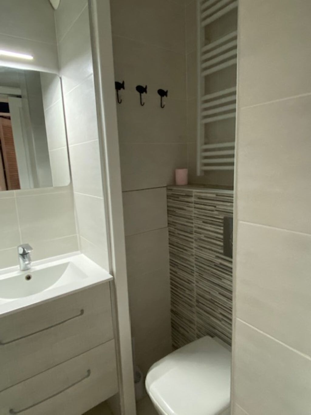 A bathroom with a white sink, mirror, and toilet. There are three hooks on the wall above the toilet.