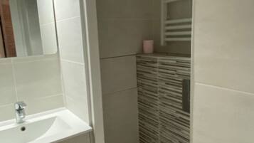A bathroom with a white sink, mirror, and toilet. There are three hooks on the wall above the toilet.