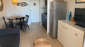 A compact kitchen with a refrigerator, a dining area with chairs and a table, and a small seating area with a sofa.