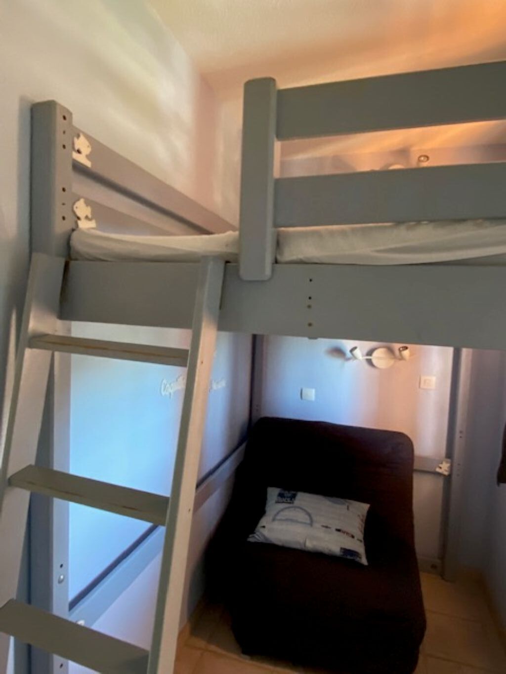 A bunk bed with a ladder, a small bedside table, and a pillow.