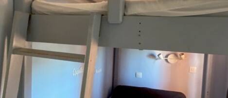 A bunk bed with a ladder, a small bedside table, and a pillow.
