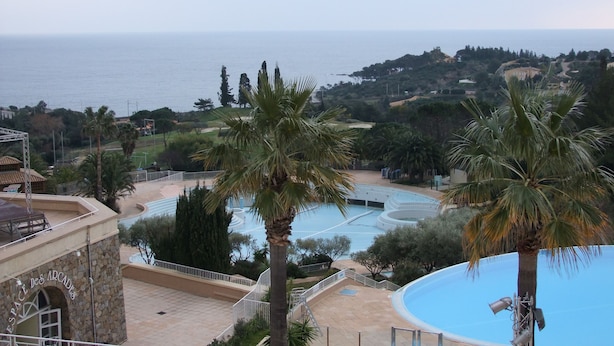 A resort with a pool, palm trees, and a view of the sea.