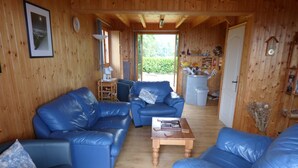 A cozy cabin interior with blue leather sofas, a wooden coffee table, and a kitchen area visible through an open door. - Beautiful Chalet for 8 people, 4 bedrooms, 3 bathrooms and beautiful views (Thollon-Les-Mémises)
