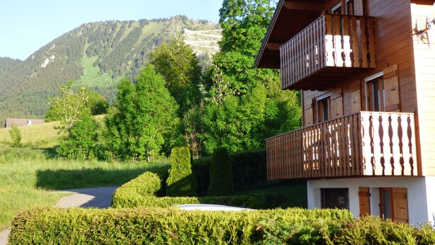 A wooden chalet with a balcony, surrounded by lush greenery and a mountain in the background. - Beautiful Chalet for 8 people, 4 bedrooms, 3 bathrooms and beautiful views (Thollon-Les-Mémises)