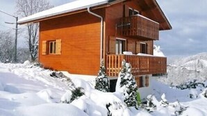 A two-story wooden cabin with a balcony, surrounded by snow-covered trees and mountains. - Beautiful Chalet for 8 people, 4 bedrooms, 3 bathrooms and beautiful views (Thollon-Les-Mémises)