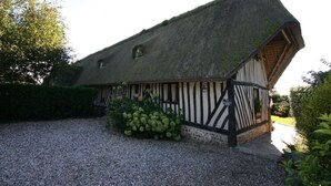 A traditional half-timbered house with a steeply pitched thatched roof, surrounded by gravel and greenery. - In the estuary of the Seine, a few minutes away from Honfleur, a real Longere (Eure)