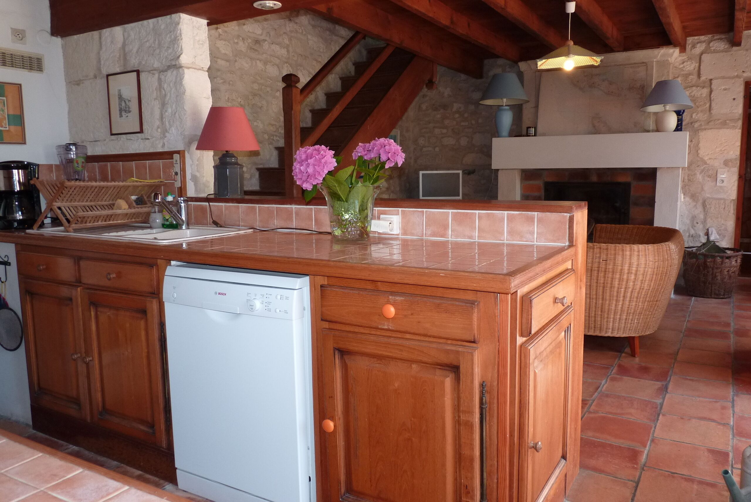 A kitchen with wooden cabinets, a dishwasher, a tiled backsplash, a vase with flowers, and a fireplace.