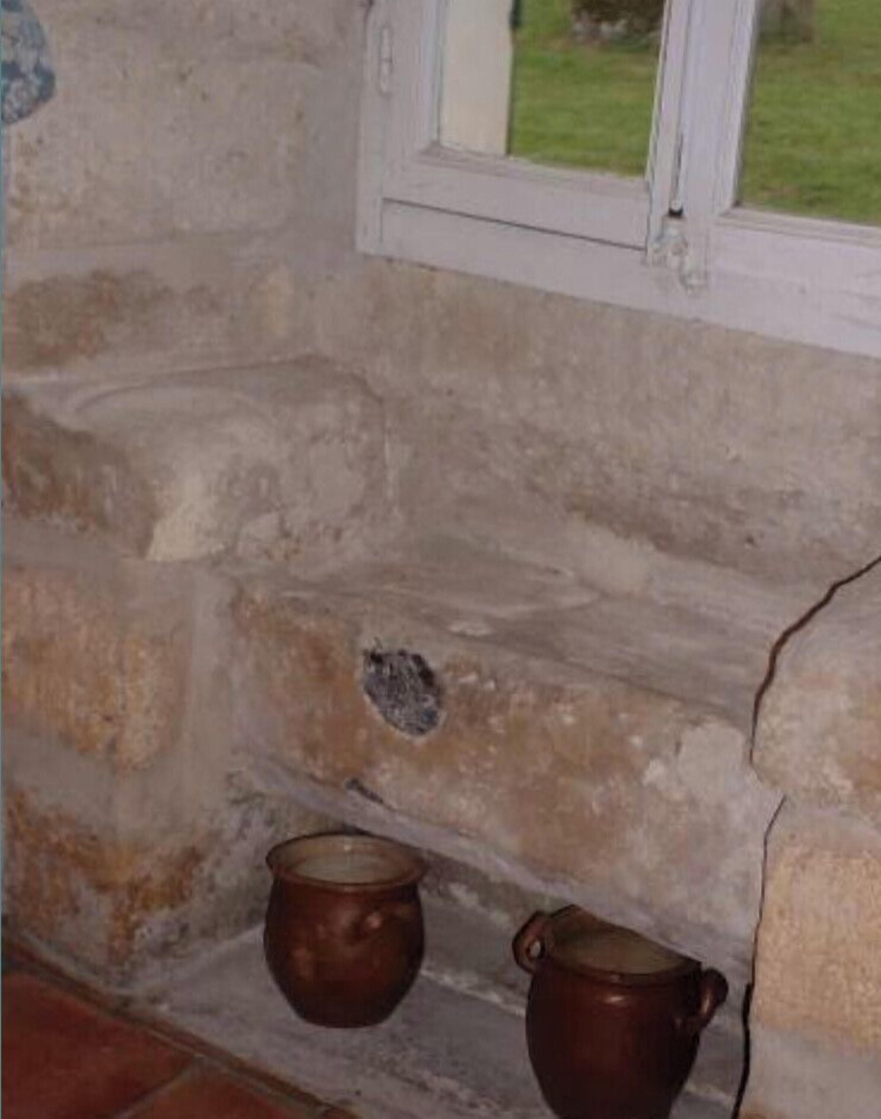 A stone wall with a window and two pots on the floor.
