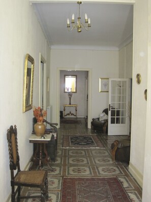 A hallway with a chandelier, a mirror, a vase with flowers, a table, a chair, a rug, and a door.