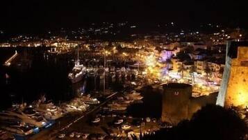 A nighttime view of a coastal town with a prominent tower and a marina filled with boats.