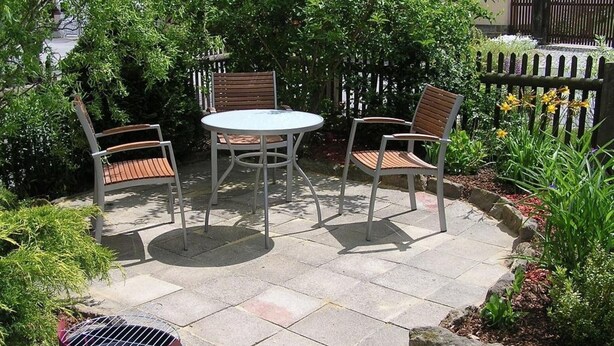 Een buitenpatio met een ronde tafel en vier stoelen, omringd door een houten hek en groen.