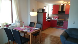Een moderne keuken met rode kastjes, een houten eettafel met stoelen, en een klein zithoekje met een raam.