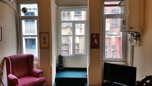 A living room with a red armchair, a television, and a window with a view of buildings. - Apartment in the Heart of the City 4 (Istanbul)
