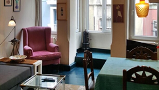 A room with a pink armchair, a glass coffee table, a chandelier, and a view of the street through large windows. - Apartment in the Heart of the City 4 (Istanbul)