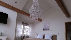 Quarto com cama grande, lustre, TV de tela plana e janela com cortinas leves.