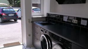 Cozinha compacta com máquina de lavar, pia e janela com vista para um estacionamento.