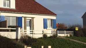 Una casa de dos pisos con techo de tejas rojas, paredes blancas y contraventanas azules.