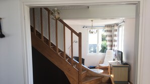 Una escalera de madera que lleva a una habitación con escritorio, silla y ventana con cortinas.