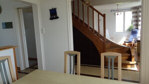Un comedor con mesa y sillas de madera, una escalera que lleva a otra habitación y una ventana con cortinas.