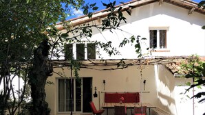 Une terrasse couverte avec une table et des chaises, un banc rouge avec coussin et une lanterne décorative.