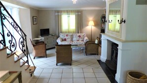 Un salon comprenant un canapé, deux fauteuils, un téléviseur, une cheminée et un escalier.