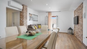 Een moderne eetruimte met een glazen tafel, stenen accentmuren, een bank met kussens en een aan de muur bevestigde televisie.