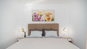 Een net opgemaakt bed met een sprei met een geometrisch patroon, een hoofdbord met een bladmotief, en een aan de muur hangend schilderij van bloemen.
