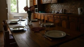 Uma cozinha com armários de madeira, uma janela ampla e uma mesa de jantar posta com pratos, copos e um vaso de flores.