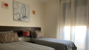 Et hotelværelse med to senge, en sengegavl, et natbord med lampe samt et billede på væggen.