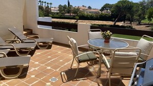 En terrasse med udendørs møbler, et bord med blomstervase og udsigt over et boligområde med træer og huse.