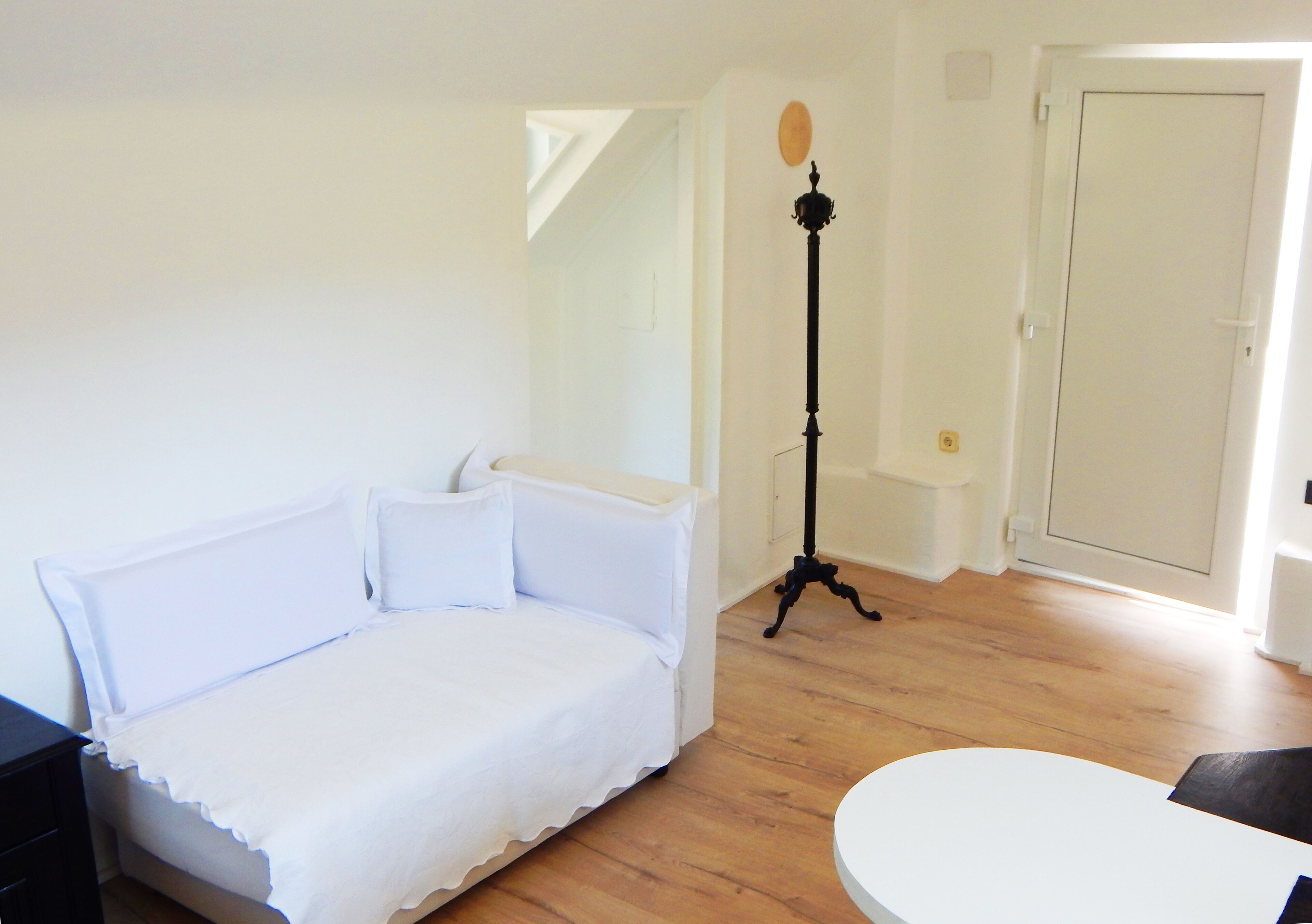 Une chambre avec un lit blanc, une petite table et une lampe sur pied.