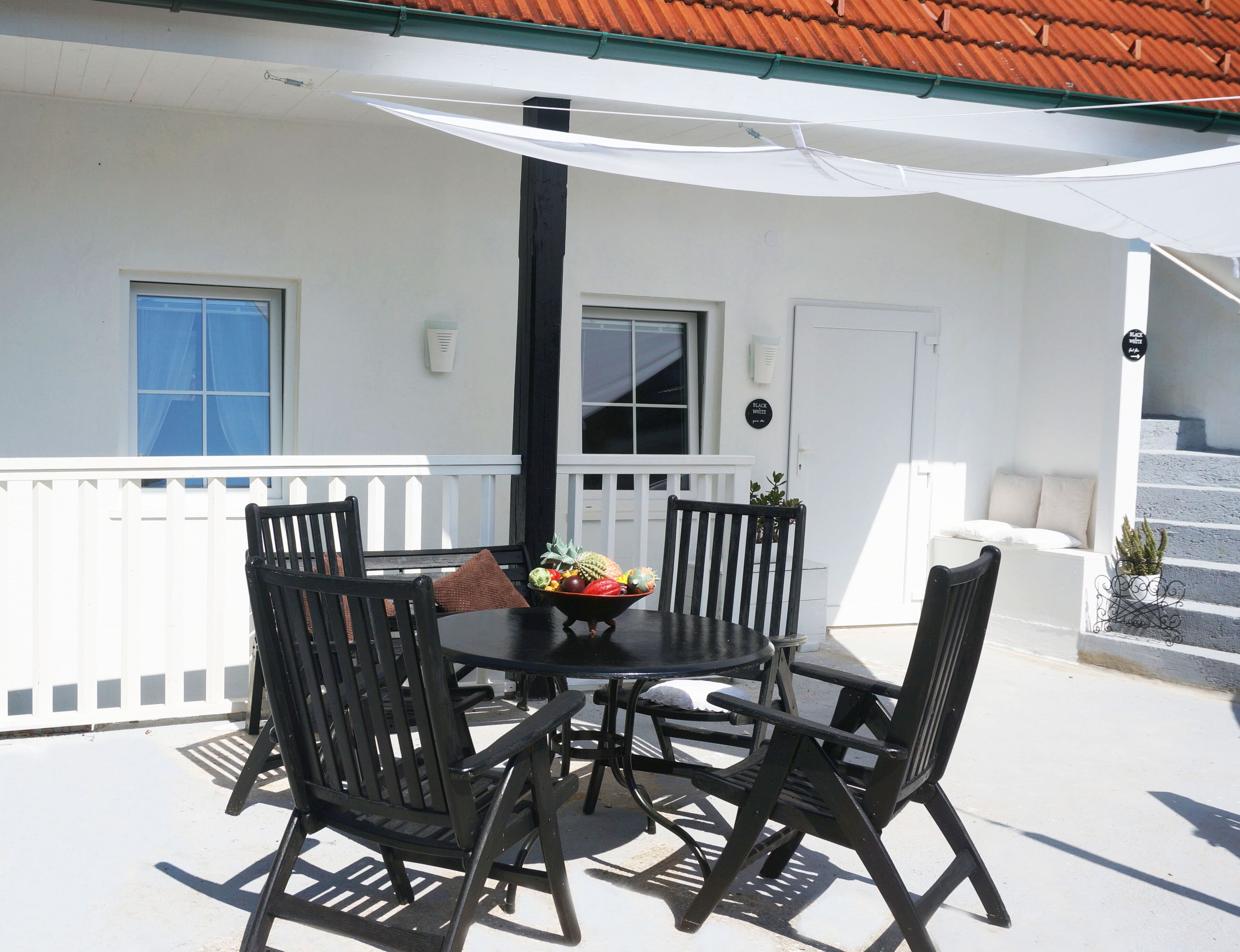 A patio with a table and chairs, a white fence, and a building with a red roof.