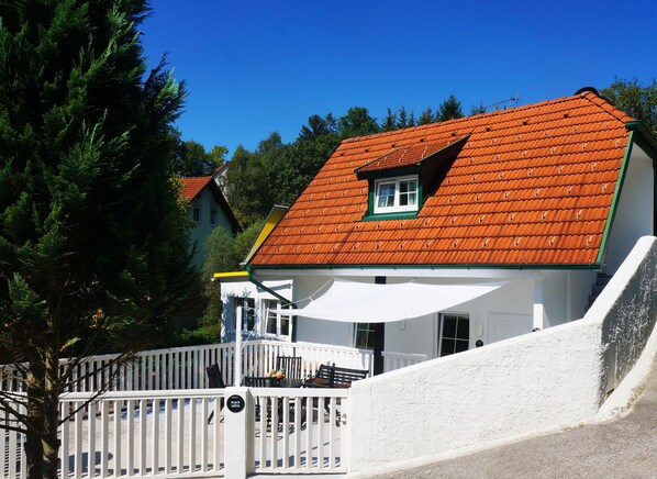 Un bâtiment blanc avec un toit recouvert de tuiles rouges, une petite fenêtre et une clôture blanche à l’avant.