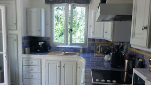 Une cuisine avec des meubles blancs, un pare-feu en carreaux, une fenêtre donnant sur un espace verdoyant, une cuisinière et un évier.