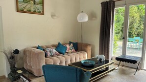 Un salon comprenant un canapé, une table basse, un fauteuil, un tableau, une lampe et une vue à travers une porte vitrée.