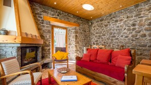A cozy living room with a stone wall, a fireplace, a wooden ceiling, and a red sofa. - Chamonix centre 2BR - Fireplace, stone walls, balcony with View of Mont Blanc (Chamonix-Mont-Blanc)