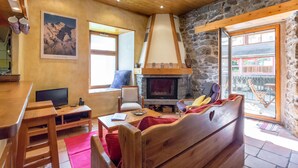 A cozy room with a stone fireplace, wooden furniture, a television, and a view of the outside. - Chamonix centre 2BR - Fireplace, stone walls, balcony with View of Mont Blanc (Chamonix-Mont-Blanc)