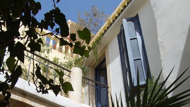 Un cortile con un edificio bianco, persiane blu e un balcone.
