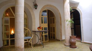 Un cortile con pavimento a scacchi, un tavolo con una ciotola di frutta, una sedia e una pianta in vaso.