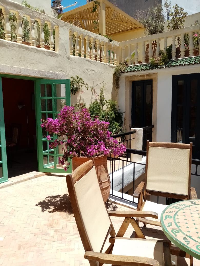 A courtyard with a wooden bench, a table, and a potted plant with pink flowers.
