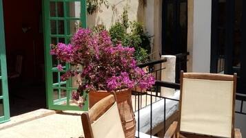 A courtyard with a wooden bench, a table, and a potted plant with pink flowers.